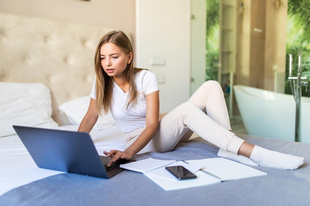 Estudio de joven mujer bonita con portátil en la cama