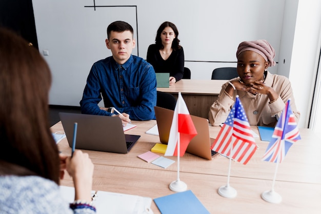 Estudio privado de la escuela extranjera con una mujer de la escuela. El maestro explica la gramática del idioma nativo usando una computadora portátil. Preparación al examen con tutor. Banderas inglesas, británicas, alemanas y polacas en el frente.