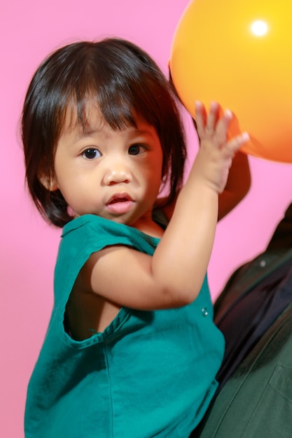 El estudio de retratos disparó a la pequeña y linda modelo de hija de una niña en edad preescolar de jardín de infantes asiático con un vestido largo informal sosteniendo globos de colores sobre fondo rosa