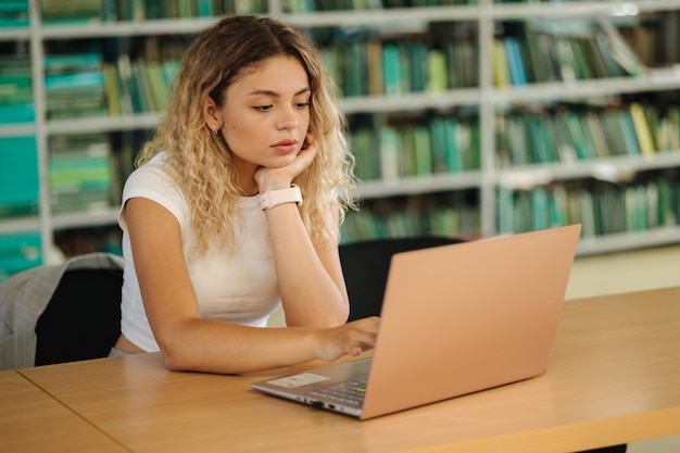 Estudo de estudante bonita na biblioteca usando laptop Vista traseira do conceito de educação de livros