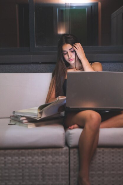 Estudo noturno de jovem mulher caucasiana no sofá do terraço. Madri, Espanha.