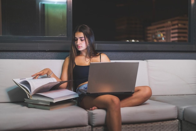 Estudo noturno de jovem mulher caucasiana no sofá do terraço. Madri, Espanha.