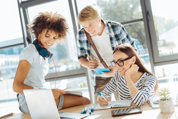 Estudo online. grupo de jovens alegres de alunos usando seus laptops e fazendo anotações enquanto estudam juntos