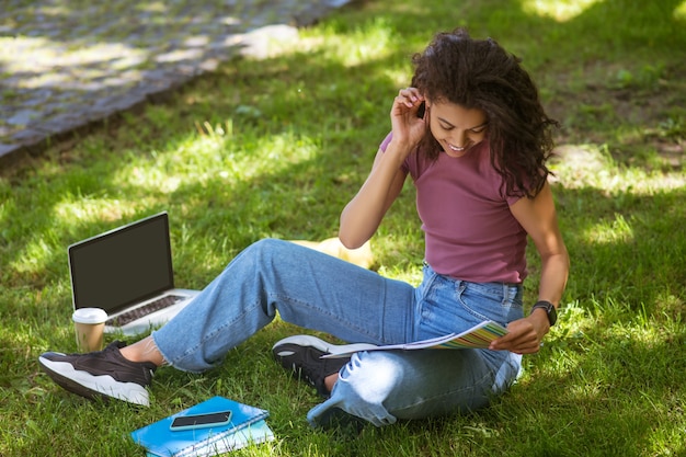 Estudo online. Uma garota com roupas casuais sentada na grama do parque e estudando