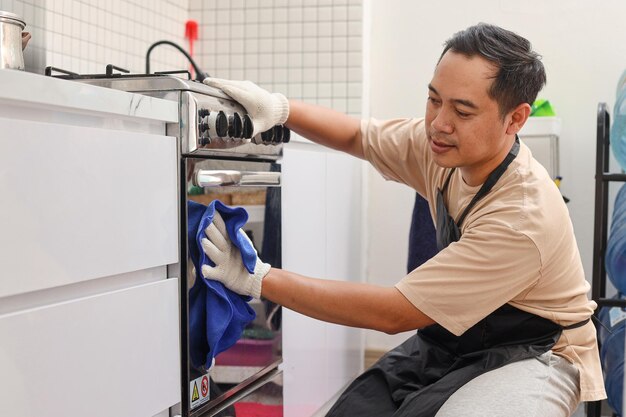 Estufa de cocina de limpieza masculina con botella de spray detergente y paño