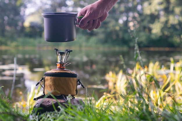 Foto estufa de gas turística para acampar y recrearse en el contexto de la naturaleza y el lago un hombre cocina comida al aire libre