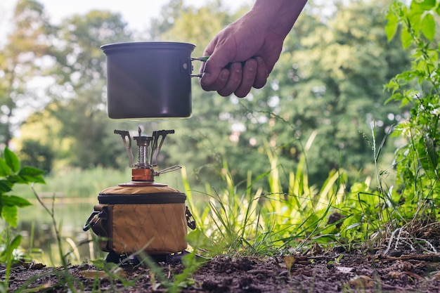 Estufa de gas turística para acampar y recrearse en el contexto de la naturaleza y el lago Un hombre cocina comida al aire libre