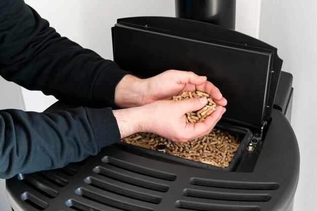 Foto estufa de pellets hombre sujetando gránulos en la mano encima de una estufa negra moderna