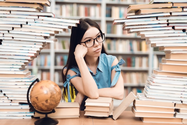 Ethnisches asiatisches Mädchen, das am Tisch sitzt, umgeben von Büchern in der Bibliothek.