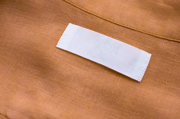 Etiqueta de etiqueta de roupa branca em branco sobre fundo de textura de tecido de camisa de linho marrom