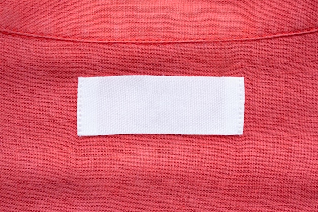 Foto etiqueta de etiqueta de roupa branca em branco sobre fundo de textura de tecido de camisa de linho vermelho