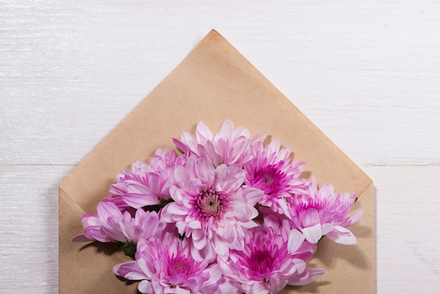 Etiqueta de papel branco em branco com envelope marrom e flores cor de rosa na mesa de madeira.