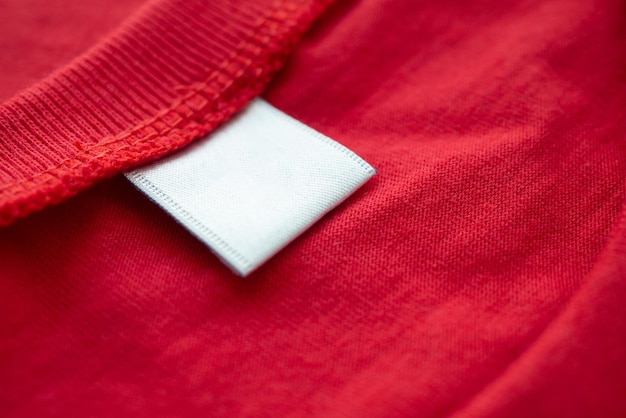 Etiqueta de etiqueta de ropa en blanco blanco sobre fondo de textura de tela de camisa de algodón rojo nuevo