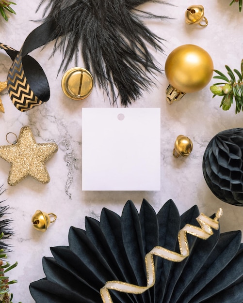 Etiqueta de regalo cuadrada en blanco entre adornos navideños negros y dorados vista superior Mockup