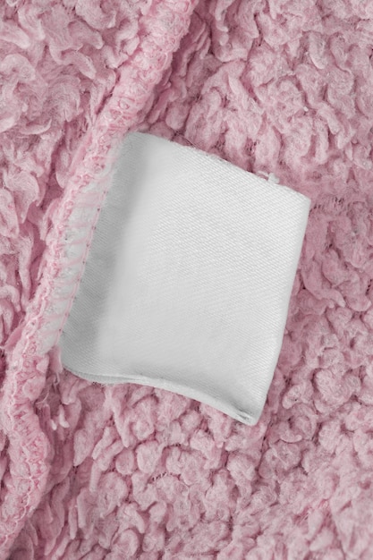 Etiqueta de ropa en blanco sobre fondo textil rosa primer plano