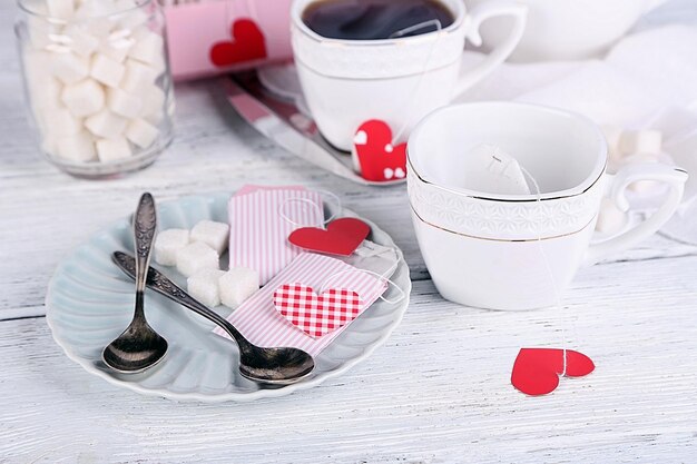 Etiquetas de bolsitas de té en forma de corazón, caja y tetera sobre fondo de madera