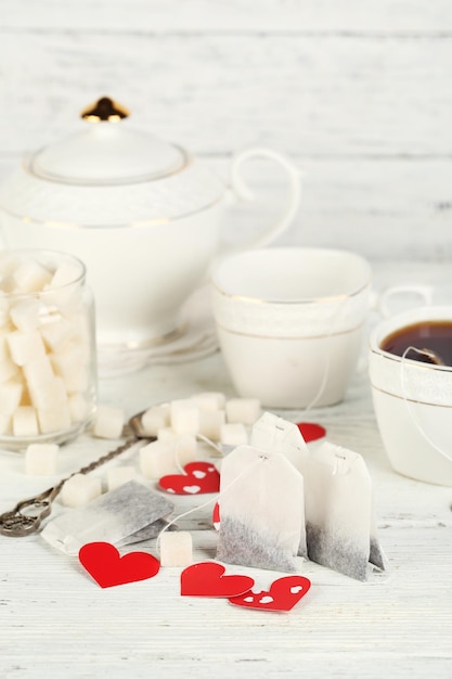 Etiquetas de bolsitas de té en forma de corazón, caja y tetera sobre fondo de madera