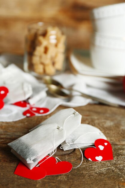 Etiquetas de bolsitas de té en forma de corazón y taza de té con fondo de madera