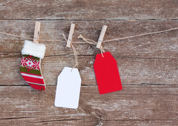Etiquetas de papel blancas y rojas y calcetines navideños colgados de una cuerda con pinzas para la ropa
