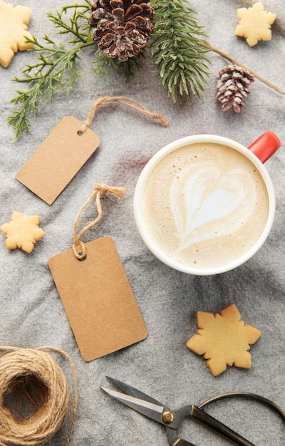 Etiquetas de regalo en blanco con taza de café de rama de pino y galletas de Navidad sobre fondo textil El concepto de preparación para las vacaciones de Navidad