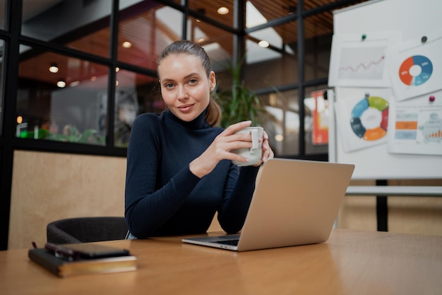 etnia sentada sola en la oficina Ella está trabajando en una computadora portátil con café en las manos