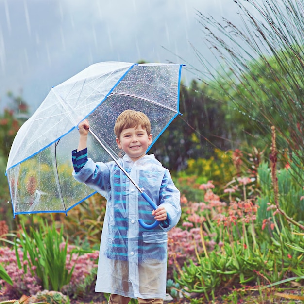 Eu amo a chuva quase tanto quanto meu jardim faz Retrato recortado de um menino do lado de fora na chuva