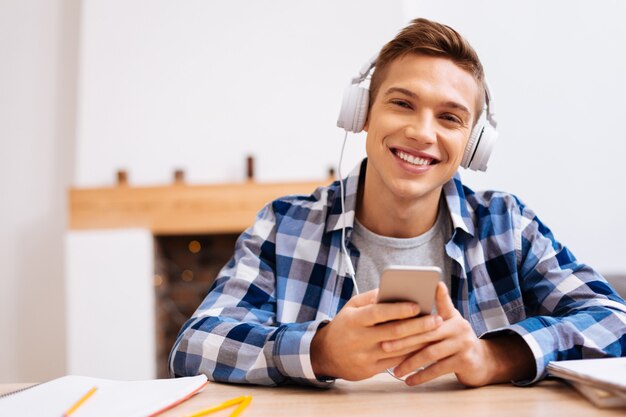 Eu amo música. Menino atraente e inspirado de cabelos louros sorrindo, usando fones de ouvido e ouvindo música