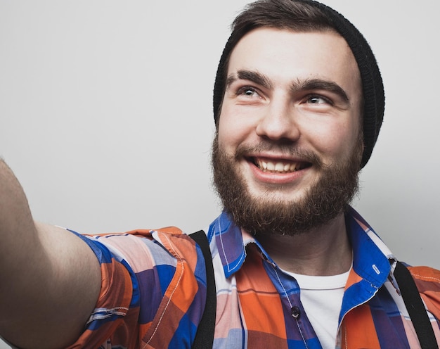 Eu amo selfie Bonito jovem barbudo segurando smartphone e fazendo selfie e sorrindo em pé contra um fundo branco