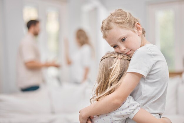 Eu era o árbitro que eles não conheciam. Foto de duas meninas abraçadas enquanto seus pais discutem ao fundo em casa.