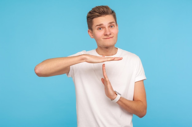 Eu preciso de uma pausa, por favor Retrato de homem trabalhador em camiseta branca casual mostrando gesto de tempo limite e pedindo para parar de implorar por pausa sem empurrar tiro de estúdio interno isolado em fundo azul