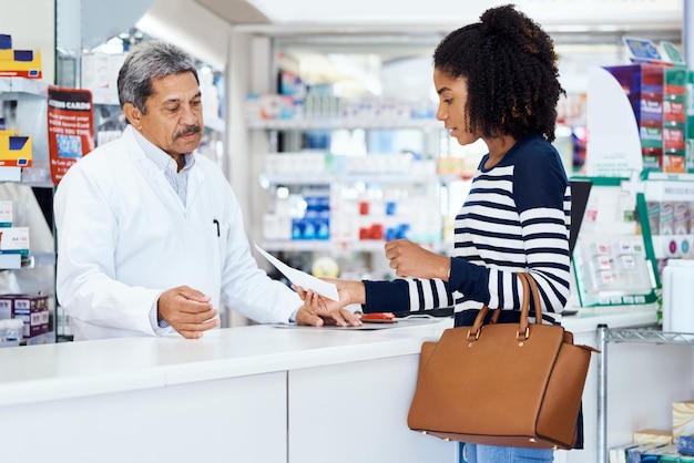 Eu preciso do seguinte medicamento, por favor Foto de um farmacêutico ajudando uma jovem em uma farmácia