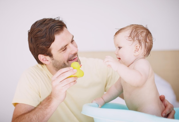 Eu quero brincar com isso Um jovem pai mostrando um brinquedo para sua filha enquanto ela está na banheira