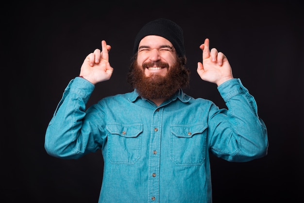 Eu quero isso. Homem alegre barbudo hippie com dedos cruzados a sonhar