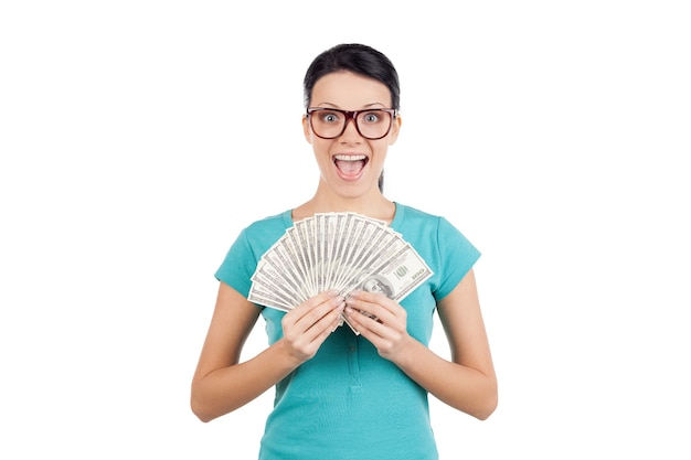 Eu sou rico! Mulher jovem feliz de óculos segurando dinheiro nas mãos e olhando para a câmera em pé, isolado no branco