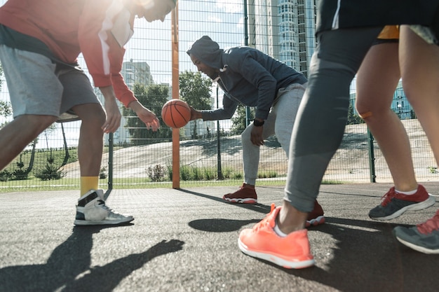 Eu tenho. Regras gratuitas. Homem forte e bom pegando uma bola com as mãos enquanto joga basquete de rua com seus amigos