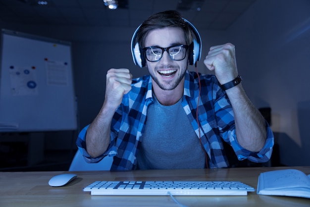 Eu venci. Homem barbudo encantado e alegre, cerrando os punhos e sorrindo enquanto ganha um jogo de computador