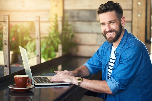 Foto eu venho aqui para o benefício do wifi gratuito retrato de um jovem bonito trabalhando em seu laptop em um café