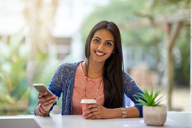 Eu venho pelo wifi, mas os cafés também são bons Retrato de uma jovem atraente usando seu celular enquanto toma café em uma cafeteria