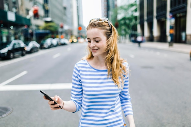 EUA, Nova York, Manhattan, jovem andando na rua, segurando o celular