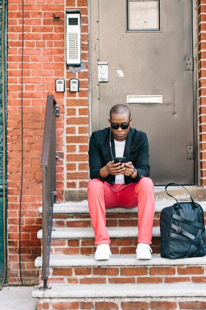 EUA, NYC, Brooklyn, homem esperando na escada, usando smartphone