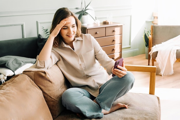 Eufórica Tech Delight Mujer millennial alegre se ríe mientras está absorta en su teléfono leyendo mensajes