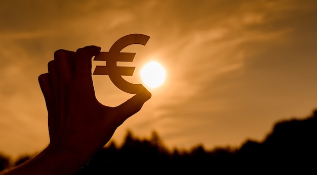 Euro-Symbol in Frauenhänden bei Sonnenuntergang konturiert. Foto in hoher Qualität