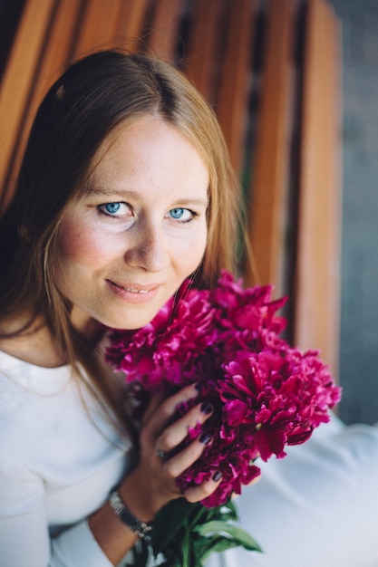 Europäisch aussehendes Mädchen mit Blumen, Pfingstrosen in ihren Händen