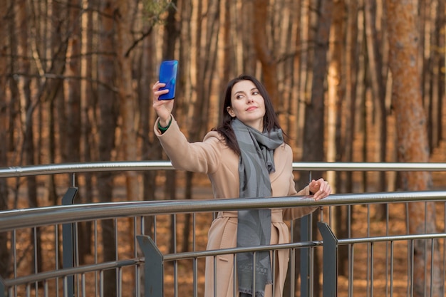 Europäische Frau im Mantel mit Telefon. Selfie machen. In der Herbststadt. Hochwertiges Foto