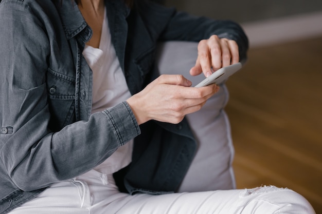 Europäische Frau von oben in einem grauen Hemd und weißen Jeans, die auf einem Stuhl sitzt und am Telefon plaudert