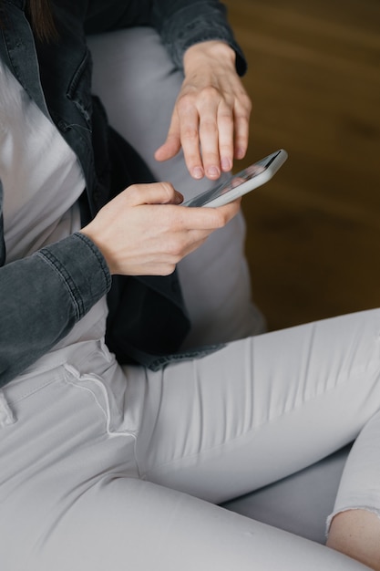 Europäische Frau von oben in einem grauen Hemd und weißen Jeans, die auf einem Stuhl sitzt und am Telefon plaudert