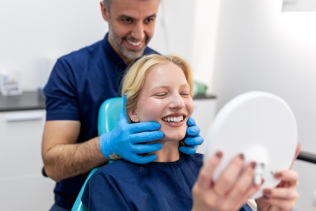 Europäische junge Frau lächelnd beim Blick in den Spiegel in der Zahnklinik Aufnahme einer jungen Frau, die ihre Ergebnisse in der Zahnarztpraxis überprüft