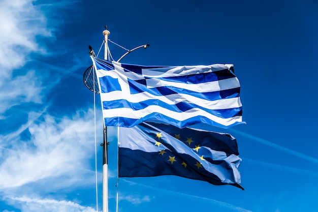 Europäische politische nachrichten grexit und nationenkonzeptflaggen von griechenland und der europäischen union auf blauem himmel hintergrundpolitik europas