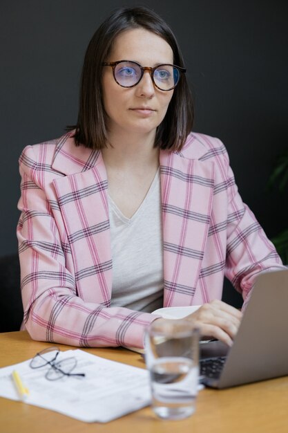 Europäische selbstbewusste Geschäftsfrau in einer rosa Jacke und mit einem Laptop in ihrem Büro arbeiten