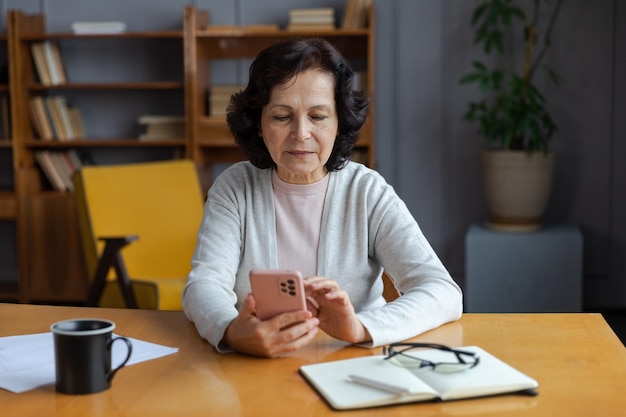 Europäische Seniorin mittleren Alters, die mit Smartphone-Touchscreen-Eingabe-Scroll-Seite hält Stilvolle ältere reife 60er-Dame mit Handy, die Internet-Social-Media-Apps zu Hause verwendet Online-Shopping